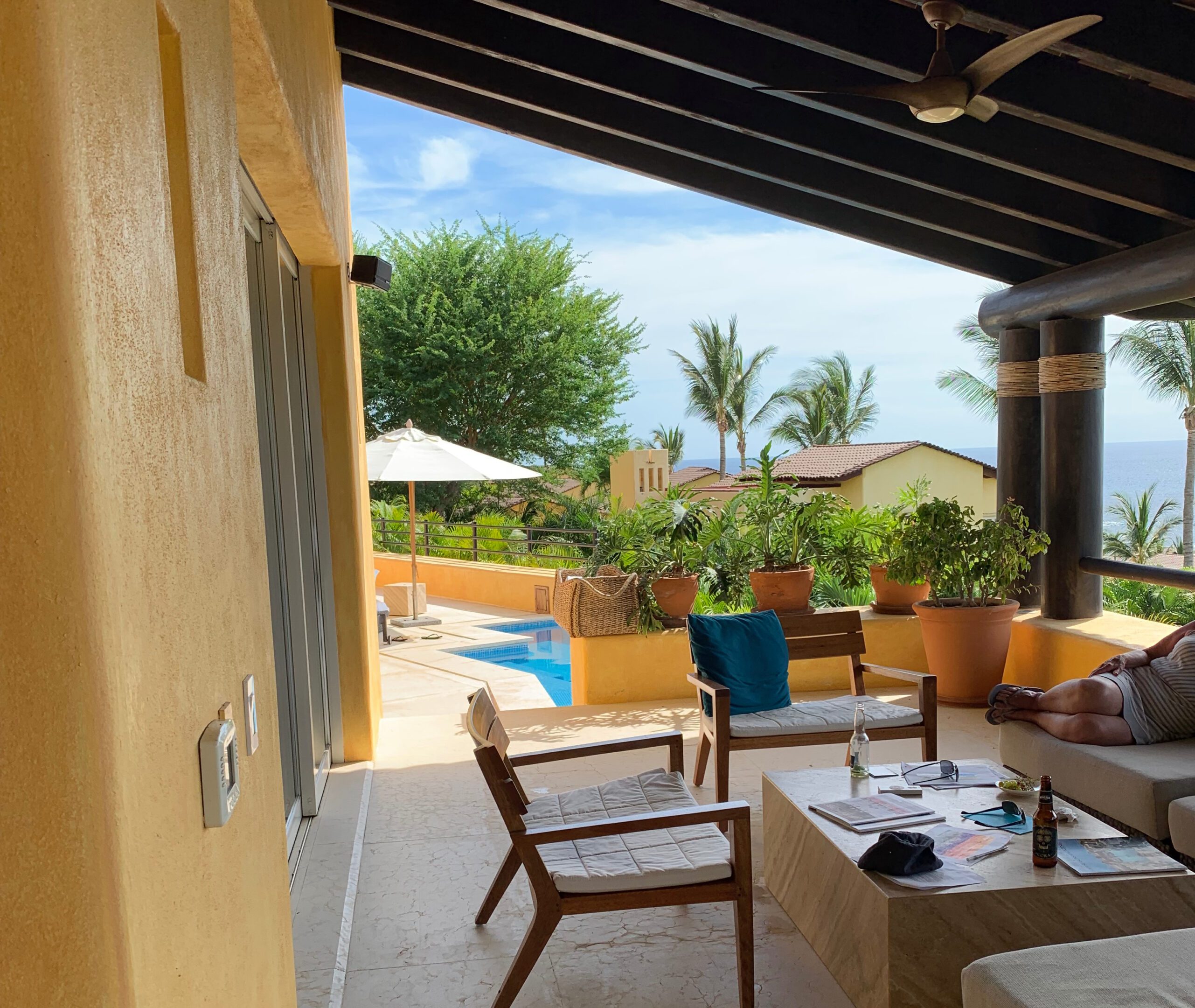 A patio with tables and chairs, pool and trees.